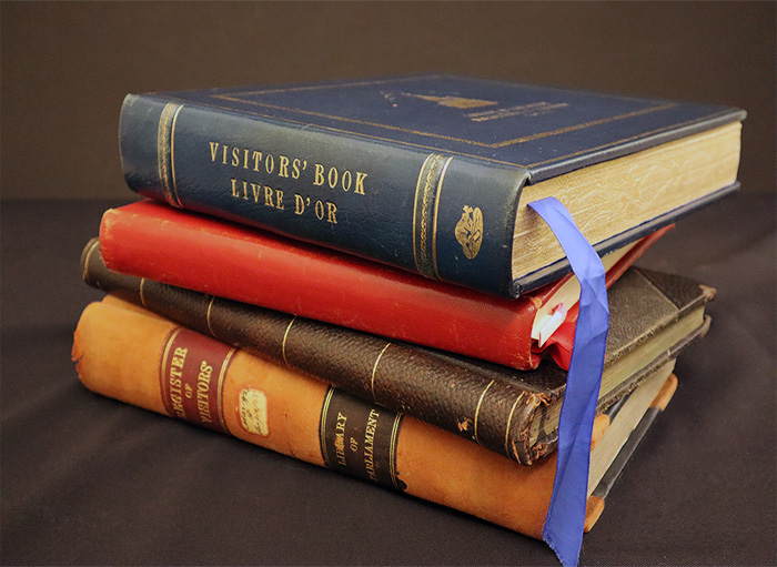4 guest books stacked on top of each other, showing their colorful leather bindings that feature gold decorations